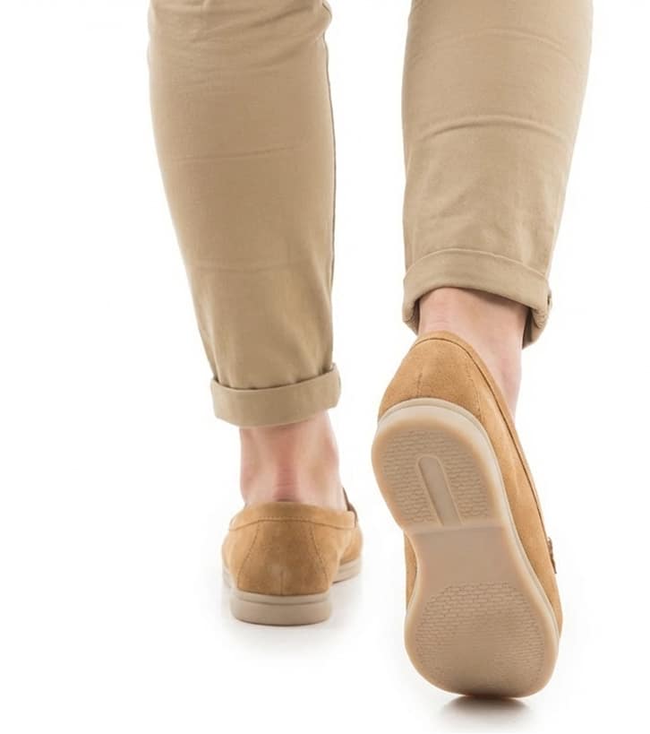 A person wearing beige pants with rolled cuffs is walking away. The focus is on the tan suede shoes and the relaxed, casual tone of the image.