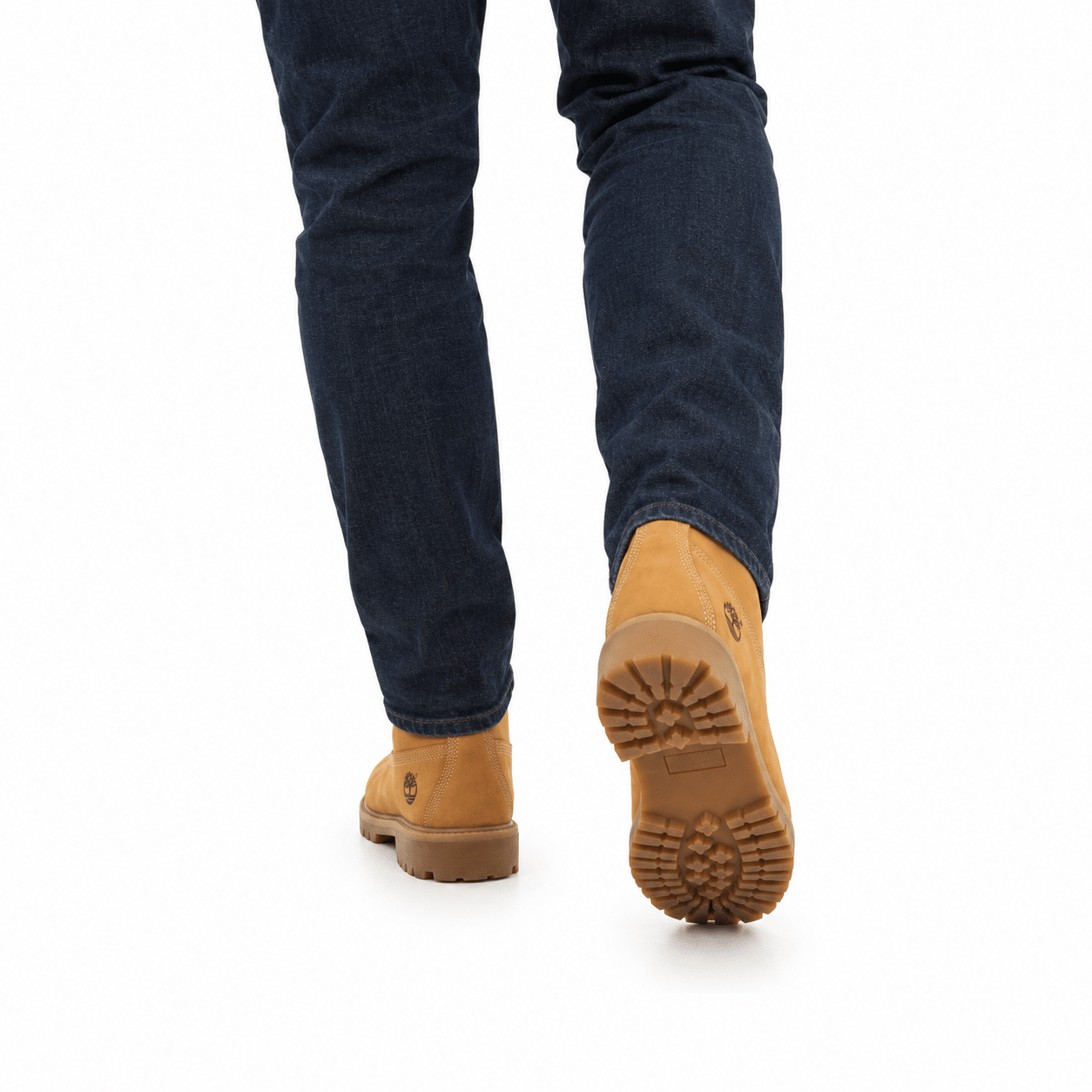Person walking in dark denim jeans and tan leather work boots on a clean white background, viewed from behind.